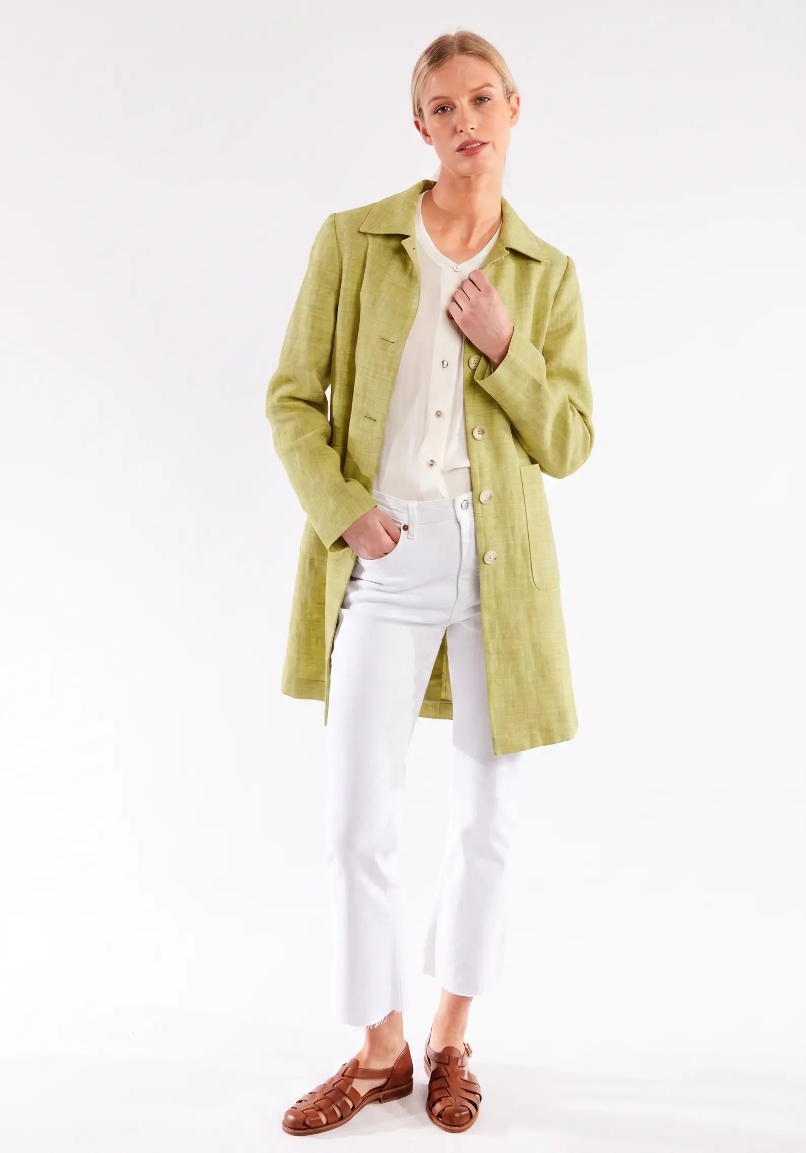 Woman wearing a green coat over a white shirt and pants on a white background