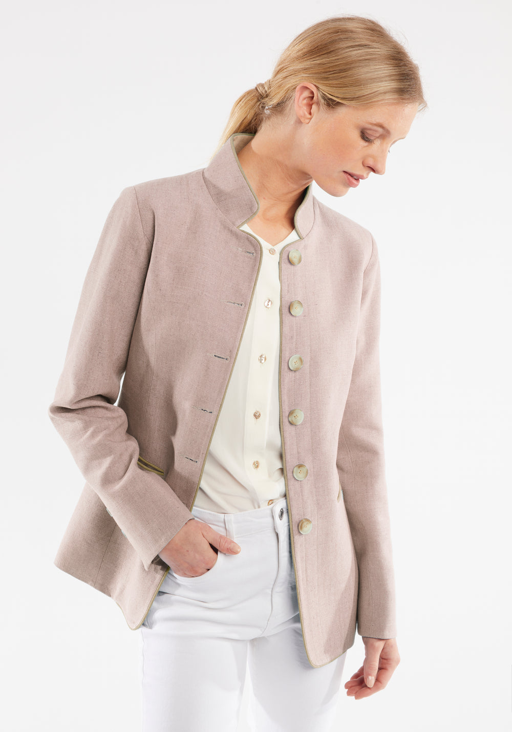 Woman wearing a light pink jacket and white pants on a white background