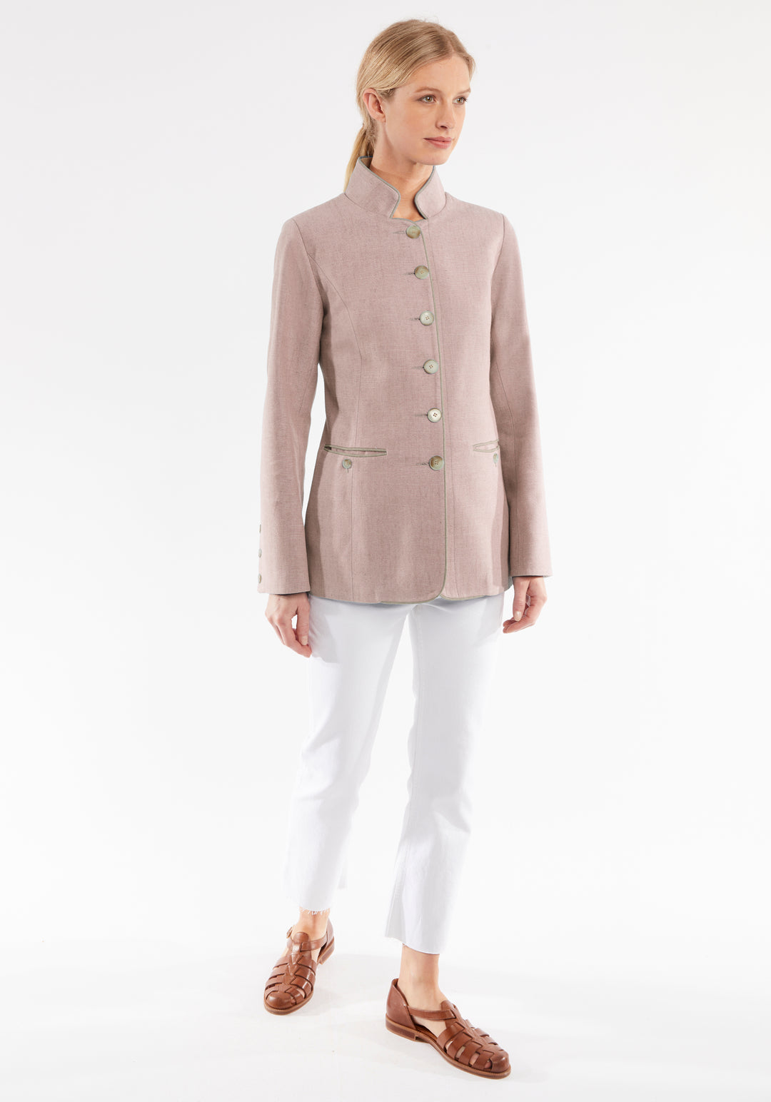 Woman wearing a light pink jacket and white pants on a white background