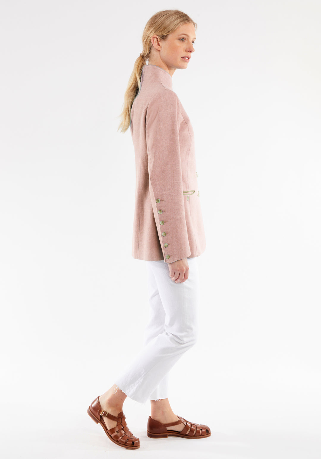 Woman wearing a light pink jacket and white pants on a white background