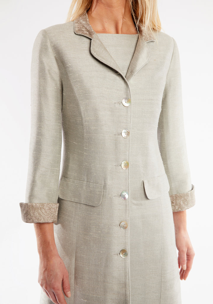 Woman wearing dove grey coat with pockets, cuff detailing and mother of pearl buttons