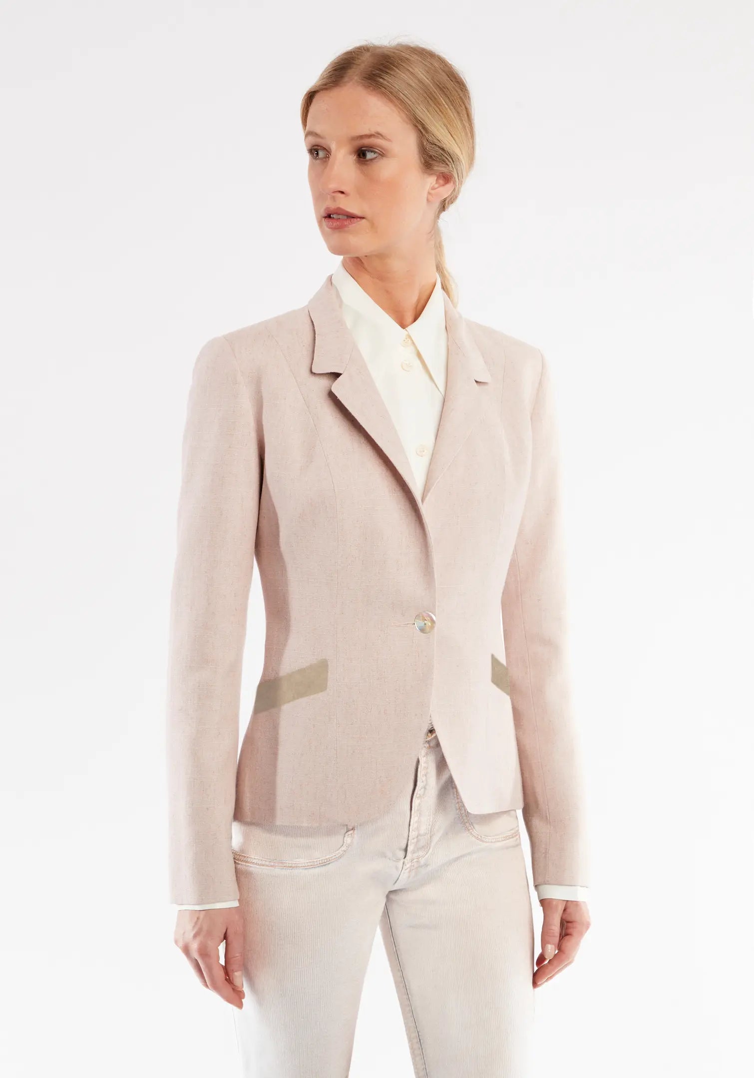 Woman wearing a light pink blazer and white pants on a white background