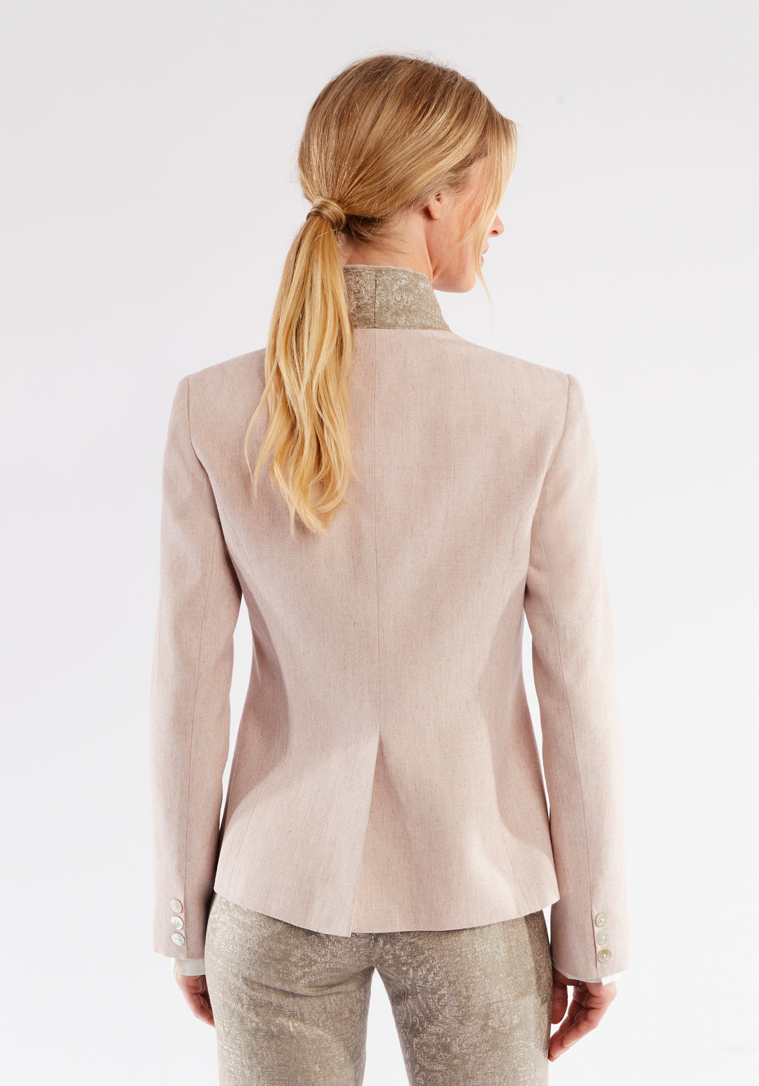 Back of a woman wearing light pink jacket with beige pocket and collar detailing