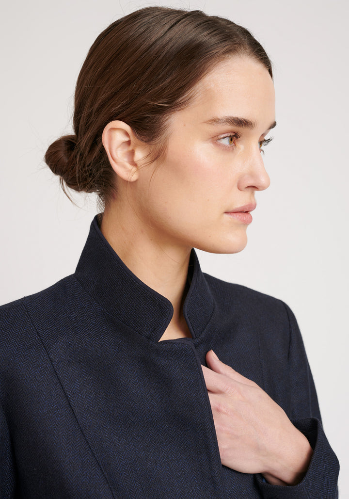 A model wears the Tallulah jacket in a smart navy and black herringbone lambswool. It has a sleek, tailored look, with a single button fastening and suede trimmed collar that can be worn up or down.